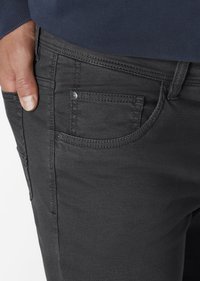 Dunkelgraue Denim-Jeans mit subtil strukturiertem Muster. Zu den Merkmalen gehören eine Vordertasche, metallische Hardware-Details und eine enge Passform an der Taille.