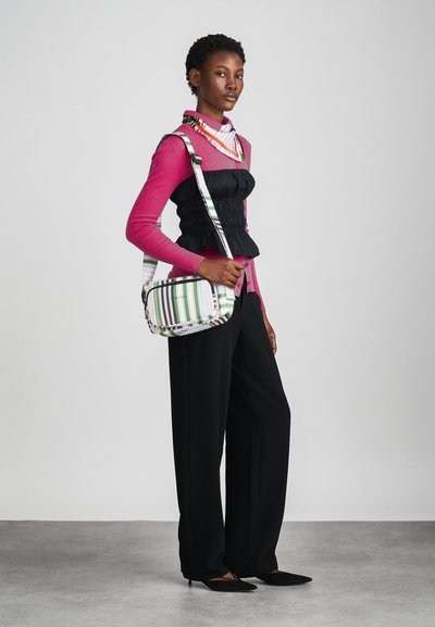 Black ruched top, pink long-sleeve shirt, wide black trousers, and a striped crossbody bag in green, white, and purple. Smooth fabric, casual design.