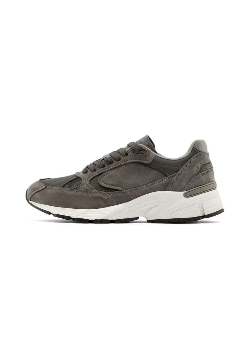 Baskets en suede gris avec semelle blanche contrastante, design à lacets, bout rond et accents texturés. Le profil latéral montre une structure de soutien.