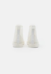 Pár bílých vysokých tenisek s poutky a logem "ALDO" na patě, zobrazené zezadu na bílém pozadí.