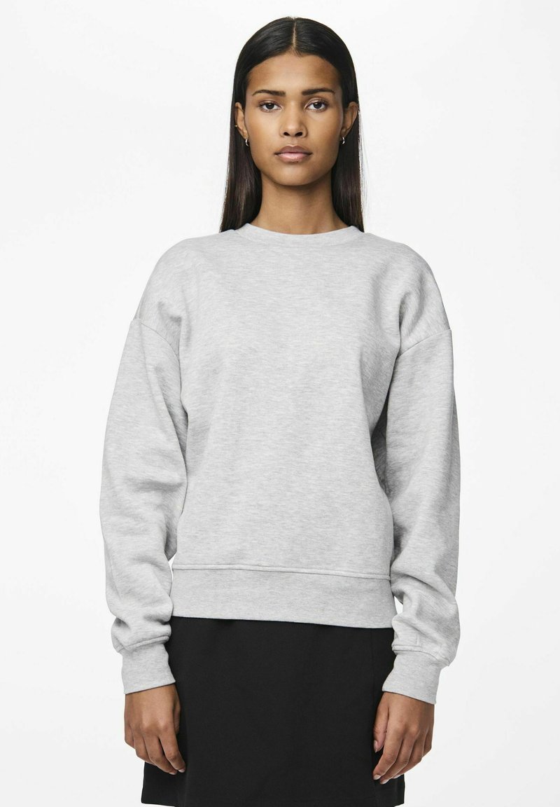 Sudadera gris de corte relajado, con mangas largas, cuello redondo y puños acanalados; combinada con una falda negra. Textura de tela suave, diseño casual.