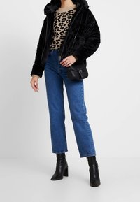 Czarna kurtka puchowa z kapturem, sweter w panterkę, niebieskie dżinsy z wysokim stanem oraz czarne botki za kostkę, do tego mała czarna torebka na ramię.