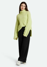 Pulover verde lime cu guler înalt, cu mâneci lungi, fante laterale; asortat cu pantaloni largi negri și adidași albi.