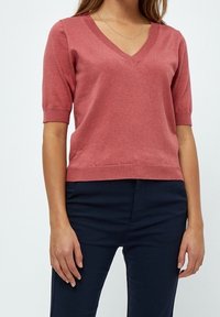 Maglione a maniche corte e scollo a V in cotone rosa. Presenta una silhouette aderente e dettagli a costine sul collo e sull'orlo. Abbinato a pantaloni scuri.