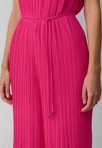 Fuchsia Faltenoverall mit geraffter Taille, der über einen Kordelzug verfügt und metallische Akzente an den Enden aufweist. Glattes, strukturiertes Material.