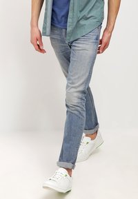 Ljusblå denimjeans med smal passform och uppvikt fåll, tillsammans med vita sneakers med gröna detaljer. Bomullsskjorta lagd ovanpå.