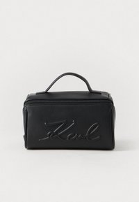 Must musta kosmeetikatuba, millel on pealmine sang, esiküljel on reljeefne logo, ristkülikukujuline vorm ja lukuga sulgemine. Sile tekstuur, minimalistlik disain.