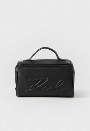 Must musta kosmeetikatuba, millel on pealmine sang, esiküljel on reljeefne logo, ristkülikukujuline vorm ja lukuga sulgemine. Sile tekstuur, minimalistlik disain.