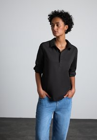 Maglietta nera a maniche lunghe con colletto e mezza abbottonatura, abbinata a jeans azzurri chiari. Tessuto morbido e vestibilità rilassata.