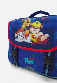 Plava torba za poruke s karakterima crtanih pasa, s crvenim obrubom i podesivim trakama, izrađena od izdržljivog materijala s glatkom teksturom.