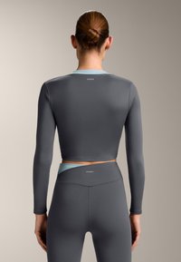 Top sportivo grigio a maniche lunghe con colletto azzurro chiaro; design aderente; tessuto liscio; logo marchiato sulla schiena. Pantaloni abbinati a vita alta.