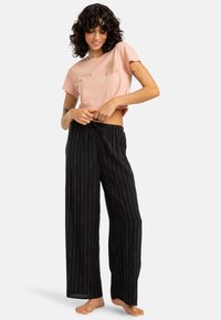 Rosa croppet t-skjorte med solgrafikk, parret med svarte bredde bukser med hvite vertikale striper og drawstring midje.