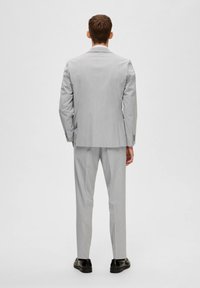 Traje gris con un corte entallado, que incluye una sola abertura, mangas largas y pantalones a juego. Unos zapatos negros completan el conjunto.