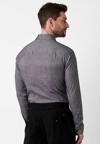 Graues Langarmhemd mit Kragen, strukturierter Stoff und Rückenpasse, kombiniert mit schwarzen, elastischen Hosen.