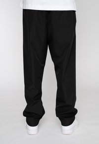 Black trousers made of lightweight fabric, featuring a loose fit and a straight cut. Paired with white sneakers for a minimalist look.
