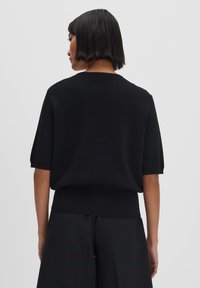 Black knitted short-sleeve sweater with a ribbed hem, featuring a round neckline and a relaxed fit. Suitable for casual wear.