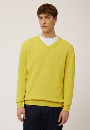 Yellow V-neck sweater in textured knit with ribbed cuffs and hem, layered over a white shirt, paired with dark blue denim jeans.