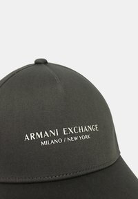 Cappellino da baseball nero con visiera curva, realizzato in materiale liscio. Presenta il logo "ARANI EXCHANGE MILANO / NEW YORK" in testo bianco sul davanti.