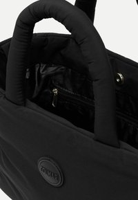 Melnā spilventiņu tote soma ar divām rokturiem, ar iešūtu iekšējo kabatu un diskrētu logo detaļu. Gluda virsma, funkcionāls dizains.
