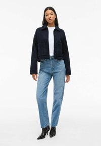 Avklippt mörkblå jacka med krage och två framfickor, i kombination med ljusblå raka jeans och svarta spetsiga klackstövlar.