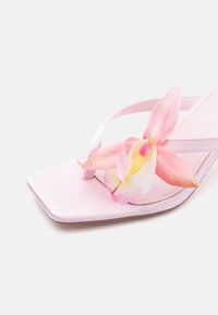 Ροζ ψηλοτάκουνο σανδάλι με τετράγωνη μύτη και ένα ροζ και κίτρινο λουλούδι ορχιδέας προσαρτημένο στο λουρί.