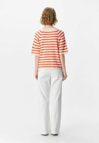 Red and cream striped short-sleeve sweater paired with white wide-leg pants. Soft, lightweight fabric with a relaxed fit and hem finishing.