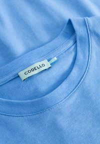 Lichtblauw t-shirt van zachte stof met een ronde halslijn en een genaaide label met de tekst "CODELLO" op de binnenkant van de kraag.