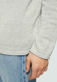 Grijze gemêleerde sweatshirt met een afgeronde zoom, geribbelde manchetten en een zijlabel, gecombineerd met lichtblauwe denim jeans.