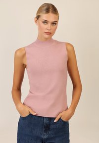 Ärmelloses pinkes Strickoberteil mit hohem Kragen, glatter Textur und figurbetontem Design; kombiniert mit blauen Jeans aus Denim mit dezenten Verzierungen.
