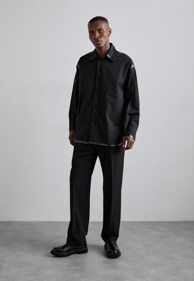 Sort kraveknap skjorte med lange ærmer og en subtil slidsemskant, parret med matchende sorte bukser og elegante sorte sko.