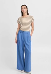 T-shirt rayé beige et marron associé à un pantalon large bleu taille haute, avec un détail de bouton et une texture douce.