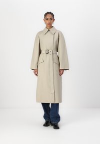 Trench bej cu guler, talie cu curea și două buzunare frontale. Mâneci largi și lungi, siluetă dreaptă. Purtat peste blugi închiși la culoare și cizme.