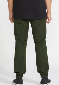 Groene joggers gemaakt van zachte stof met een taps toelopende pasvorm, elastische boorden en zijzakken, gecombineerd met zwarte casual schoenen.