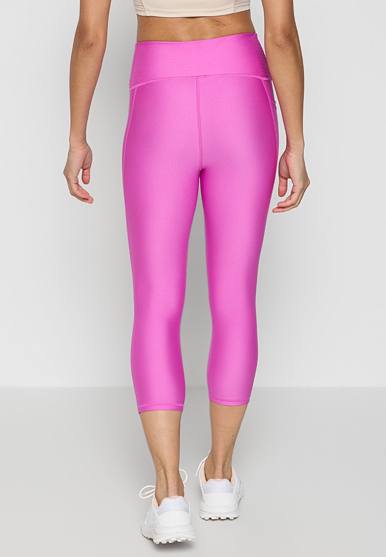 Leggings capri fucsia con una texture liscia, vita alta e cuciture piatte, abbinati a scarpe da ginnastica bianche.