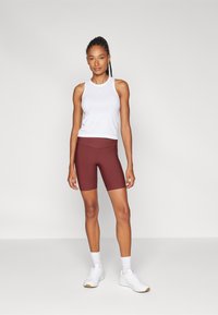 Top bianco senza maniche e pantaloni bici bordeaux. Il top ha un collo rotondo e i pantaloni presentano una superficie liscia e un design aderente.