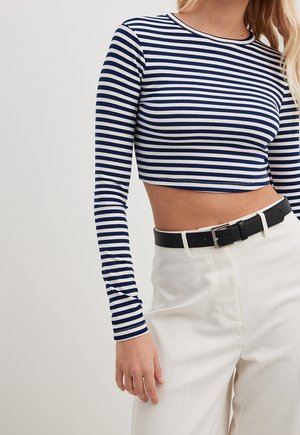 Kvinde iført en navy- og hvidstribet langærmet crop top med hvidtaljede bukser og et sort bælte med sølvspænde.