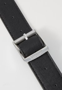 Zwarte leren riem met een gestructureerde afwerking, voorzien van een zilveren metalen gesp met een geribbelde rand en de merknaam "Desigual" gegraveerd.