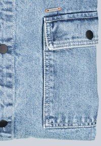 Hellblaues Denim-Jacket mit einer großen Fronttasche und schwarzen Druckknöpfen. Der Stoff hat eine weiche Textur mit verwaschenen Akzenten.