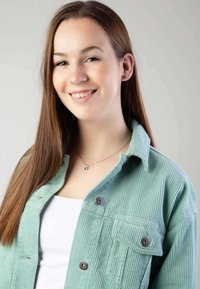 Muntgroene corduroy button-up jas met een ribbeltextuur, voorzien van bruine knopen en een borstzak. Draagt over een witte top.