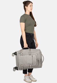 Graue Stoff-Reisetasche mit Rollen, Reißverschlusstaschen und Griffen. Strukturierte Oberfläche mit verstellbaren Gurten und modernem Design.