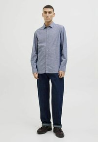 Cămașă albastră deschis, cu mâneci lungi și guler, asortată cu blugi largi, de culoare albastră închisă și pantofi negri cu șiret. Design simplu, fără modele.