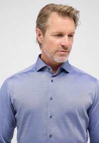 Blauwe blouse met knopen en een subtiel gestructureerd patroon, lange mouwen en een kraag. Beschikt over contrasterende patroon details aan de binnenkant van de kraag.