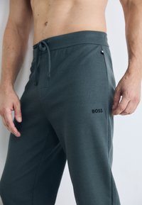 Graue gemusterte Jogginghosen mit einem Gummizugbund und einer Seitentasche. Mit einem schwarzen "BOSS"-Logo am unteren Bein.