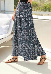 Jupe maxi légère à motif en bleu marine, blanc et turquoise avec une fente sur le côté, associée à des sandales plates noires sur une surface lisse.