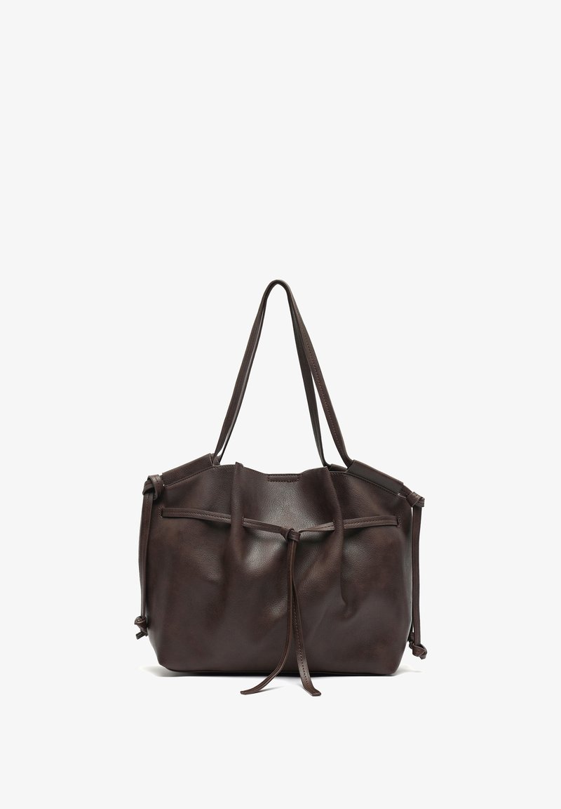 Ciemnobrązowa torba typu tote ze skóry o miękkiej fakturze, ściąganym górnym brzegiem i dwoma długimi uchwytami. Z boku ozdobiona wiązaniami.