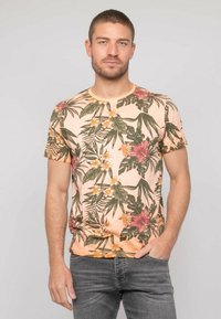 T-shirt à manches courtes de couleur pêche avec un motif floral tropical en vert, rose et jaune. Tissu en coton doux, encolure ronde, coupe régulière.