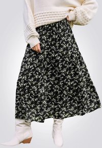 Jupe maxi noire à fleurs, ornée de fleurs blanches et vertes, design à volants, tissu doux, assortie à des bottines blanches.