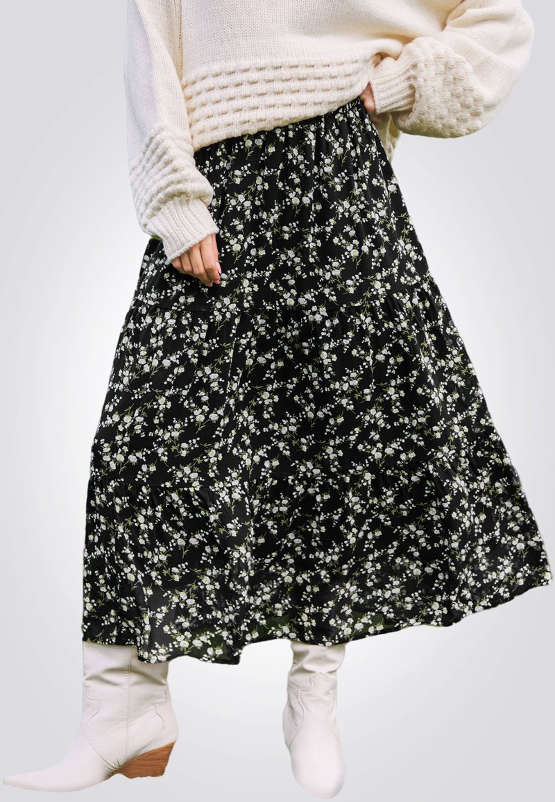 Jupe maxi noire à fleurs, ornée de fleurs blanches et vertes, design à volants, tissu doux, assortie à des bottines blanches.