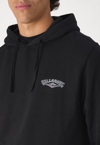 Black hoodie made of soft cotton material, featuring a colorful embroidered logo on the chest and drawstrings on the hood.