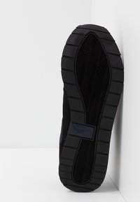 Semelle de basket noire en caoutchouc texturé, présentant un motif en chevrons. Comprend un patch de marque portant l'inscription "HACKETT LONDON" en bleu.